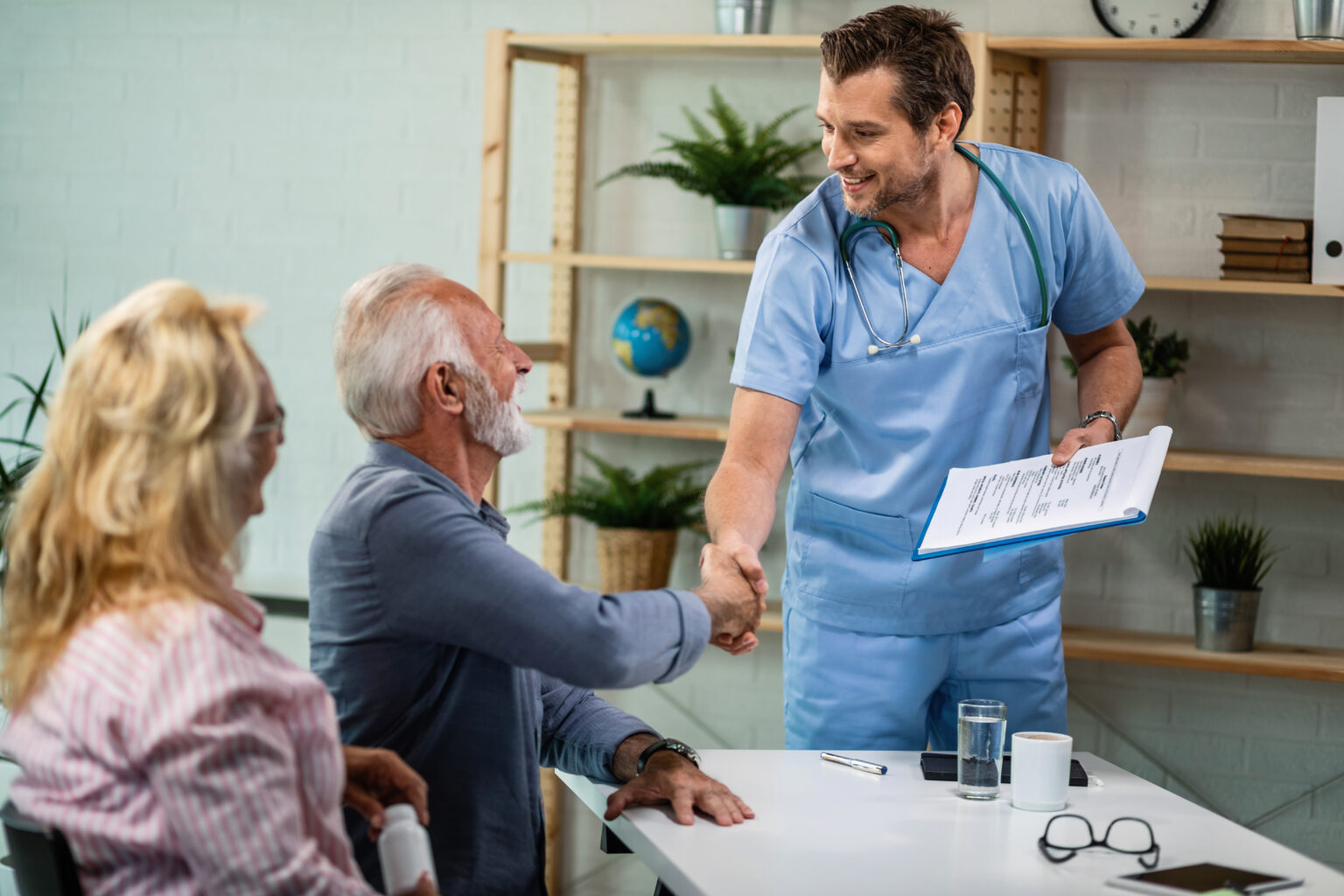 happy doctor greeting senior couple who came to medical appointment.
